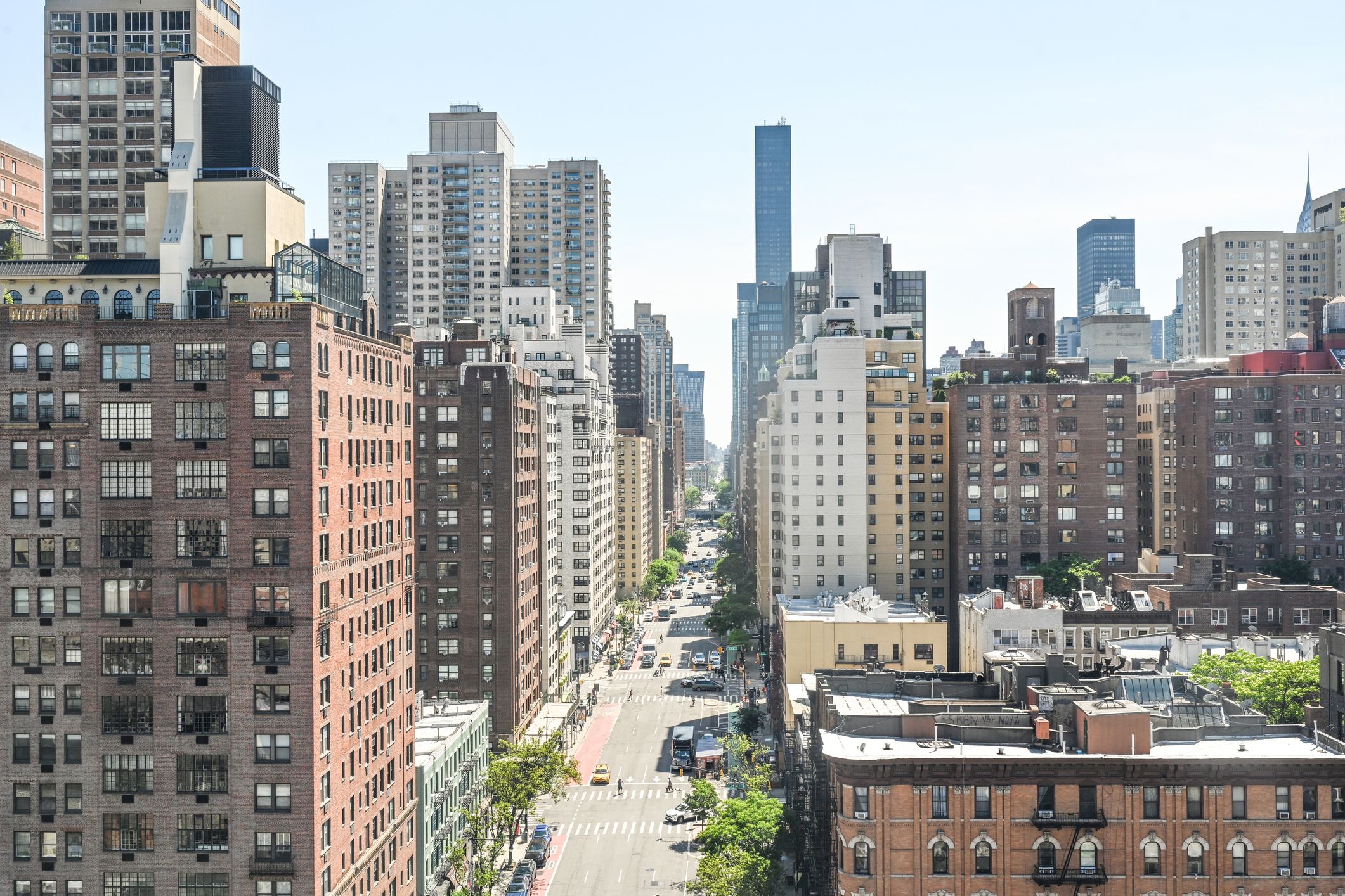 Aerial view down First Avenue in Manhattan showing trees, cars, and pedestrians surrounded by a variety of tall buildings